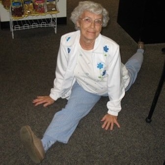 A gray-haired woman in her 70's poses doing the splits for the camera.